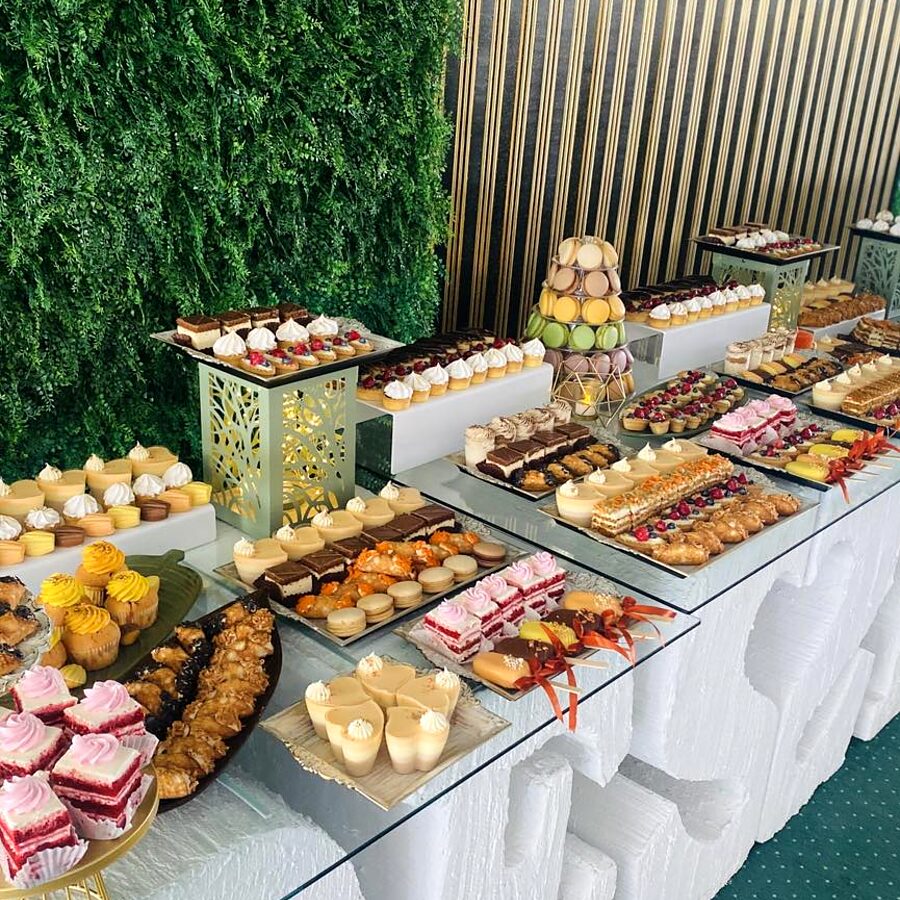 Masă de candybar cu perete verde în spate, plină de mini-prăjituri