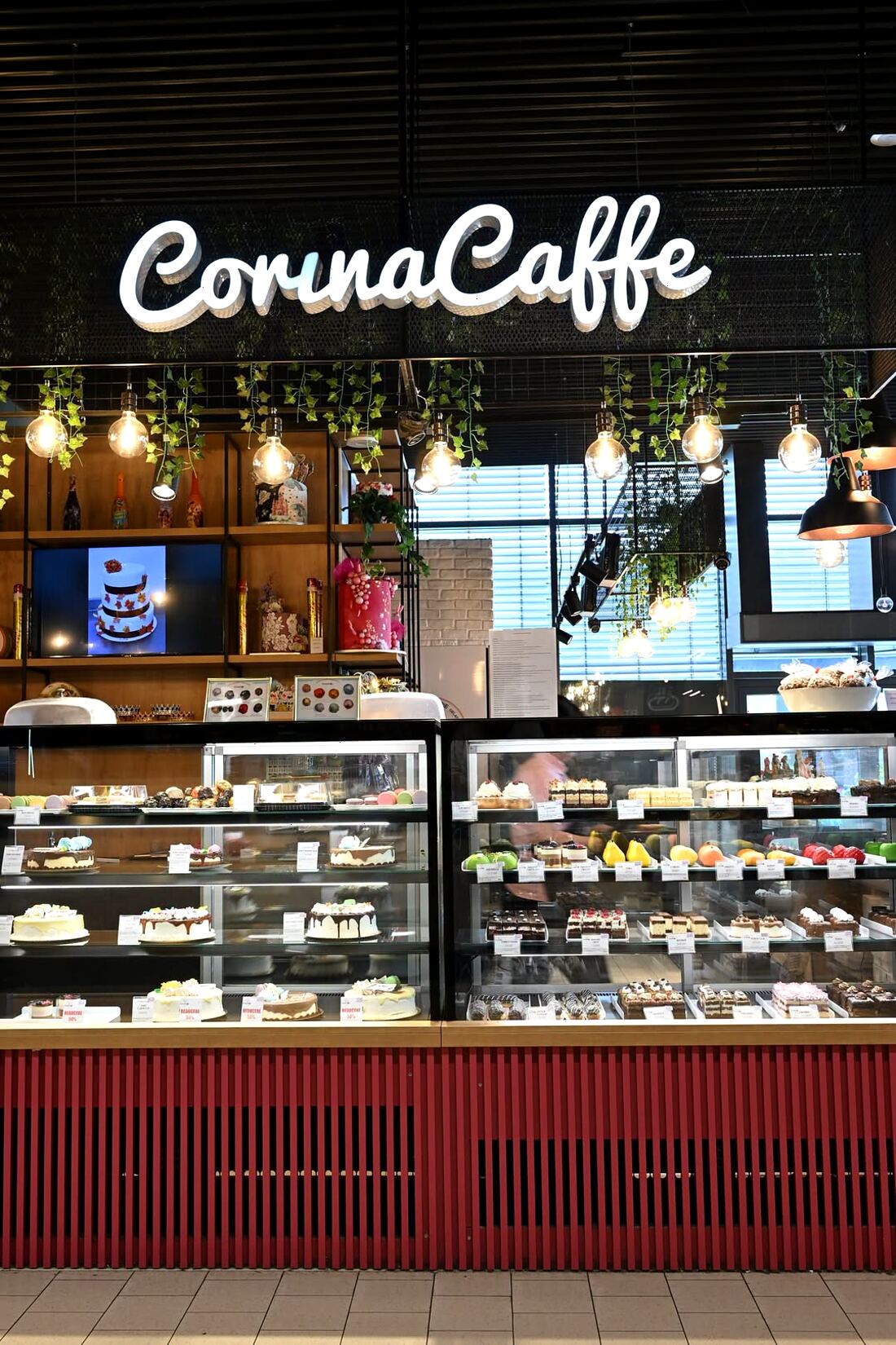 Vitrina Corina Caffe seara, cu firma luminoasă, becuri suspendate și vitrine pline de prăjituri
